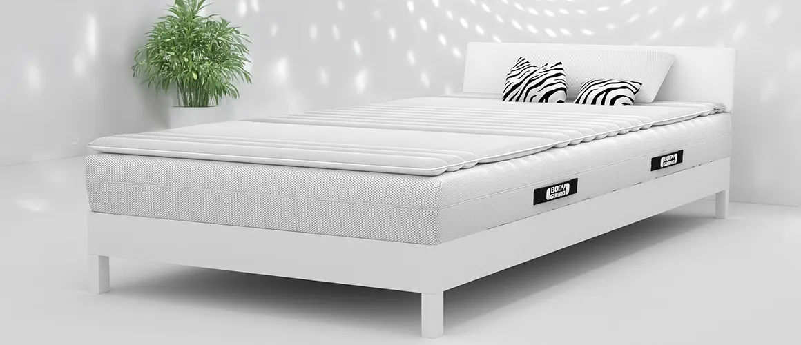 Białe pomieszczenie z białym łóżkiem, na którym leży materac BODYGUARD, topper oraz poduszka.