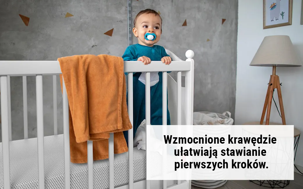 Dziecko stoi w łóżeczku. Tekst: Wzmocnione krawędzie ułatwiają stawianie pierwszych kroków.