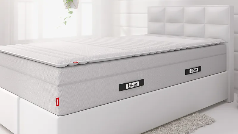 Fragment białej sypialni z łóżkiem i materacem BODYGUARD Boxspring oraz topperem.