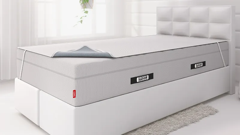 Fragment sypialni z łóżkiem i materacem BODYGUARD Boxspring i nałożoną nakładką higieniczną.