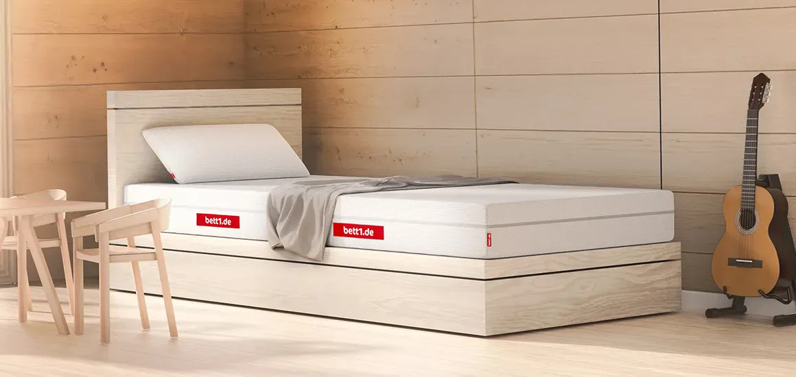 Niskie łóżko z materacem BODYGUARD oraz poduszką. Obok po prawej stronie gitara oparta o ścianę.