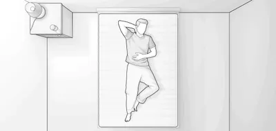 Ilustracja przedstawia sypialnię z lotu ptaka. Mężczyzna leży na plecach na materacu. obok po lewej stronie stolik nocny z lampką.