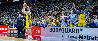 Członek drużyny Alba Berlin wrzucający piłkę do kosza podczas meczu.