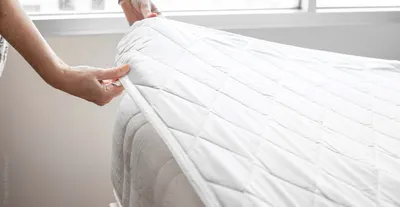 Osoba zakładająca pikowany ochraniacz na materac